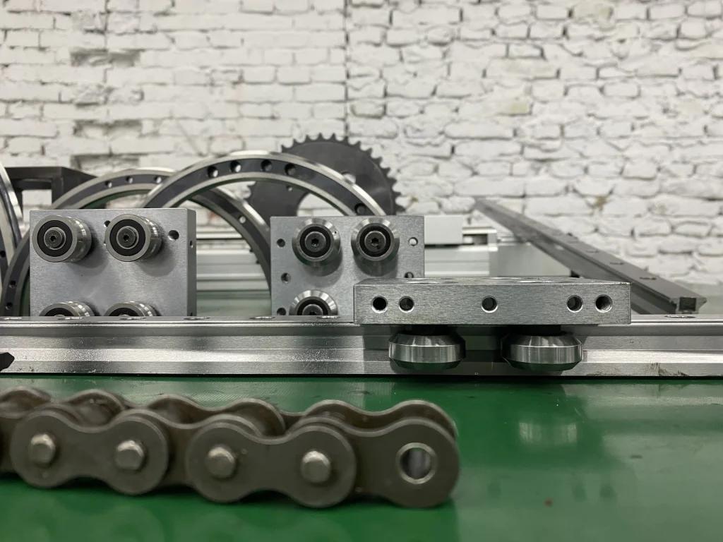 Roller carriage plates, straight guide sections and a chain displayed on a workbench